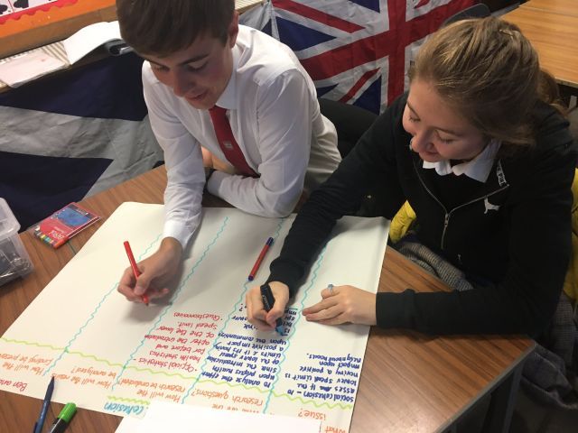 Two school pupils at a desk writing on a large sheet of paper